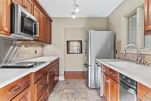 kitchen with brown cabinetry, decorative backsplash, stainless steel appliances, light countertops, and a sink