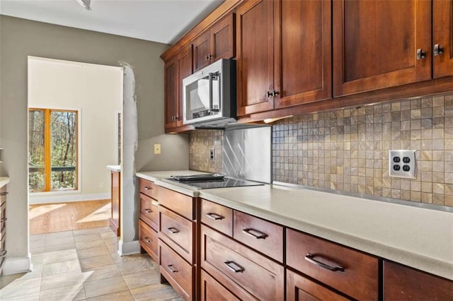 kitchen with baseboards, decorative backsplash, stainless steel microwave, black electric stovetop, and light countertops