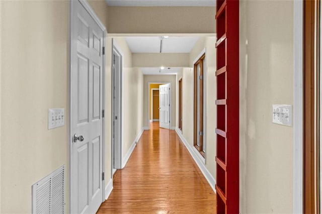 hallway featuring baseboards, visible vents, and light wood finished floors