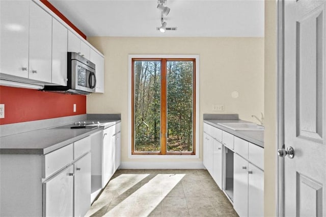 kitchen featuring white cabinets, stainless steel microwave, a sink, and light tile patterned floors