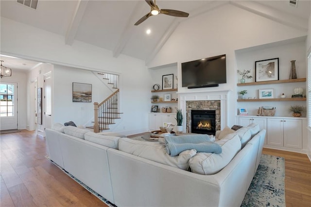 living room with visible vents, beamed ceiling, stairway, ceiling fan with notable chandelier, and light wood-style floors