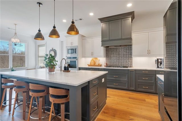kitchen with visible vents, an island with sink, stainless steel appliances, light wood-style floors, and backsplash