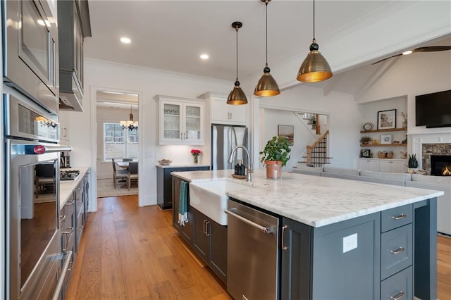 kitchen with a sink, open floor plan, stainless steel appliances, light wood-style floors, and glass insert cabinets