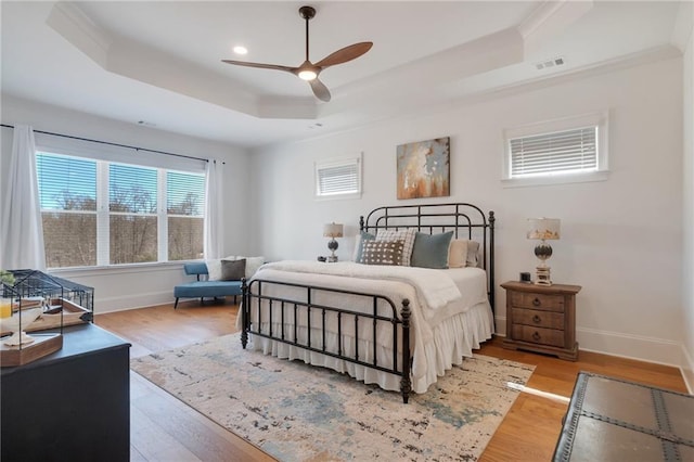 bedroom featuring visible vents, baseboards, a tray ceiling, and wood finished floors