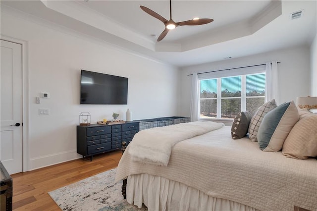 bedroom with a ceiling fan, baseboards, visible vents, a tray ceiling, and light wood-style flooring