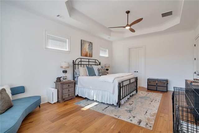 bedroom featuring a tray ceiling, light wood-style floors, visible vents, and a ceiling fan