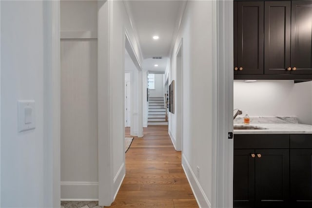 corridor with visible vents, baseboards, recessed lighting, light wood-style flooring, and a sink