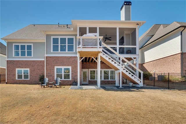 rear view of house featuring a yard, brick siding, stairs, and fence