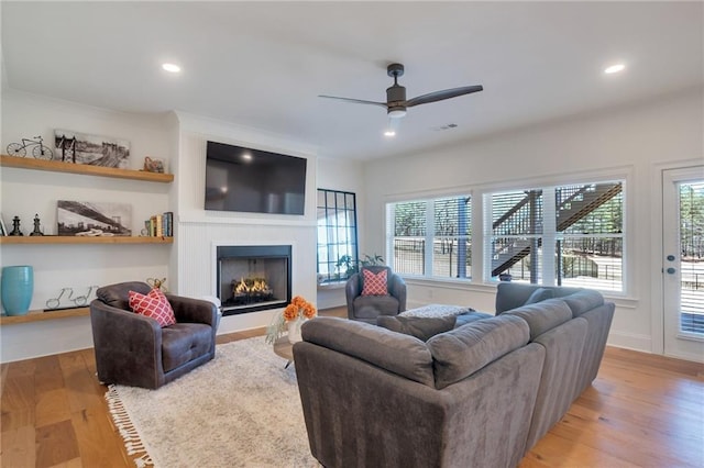 living room with a wealth of natural light, wood finished floors, a warm lit fireplace, and ceiling fan