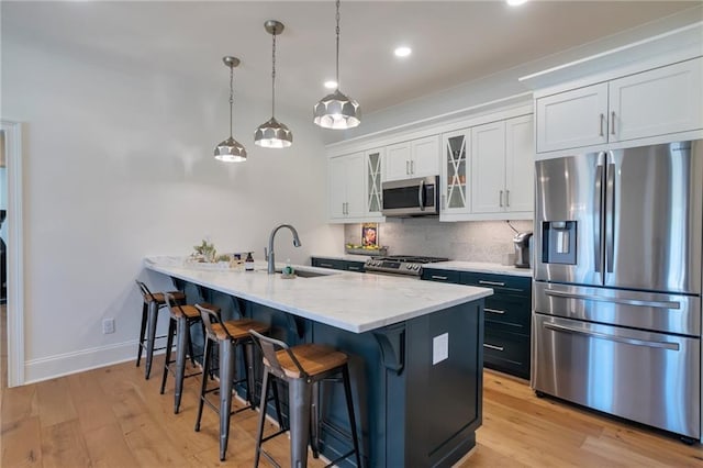 kitchen featuring a breakfast bar, a sink, tasteful backsplash, appliances with stainless steel finishes, and light wood finished floors