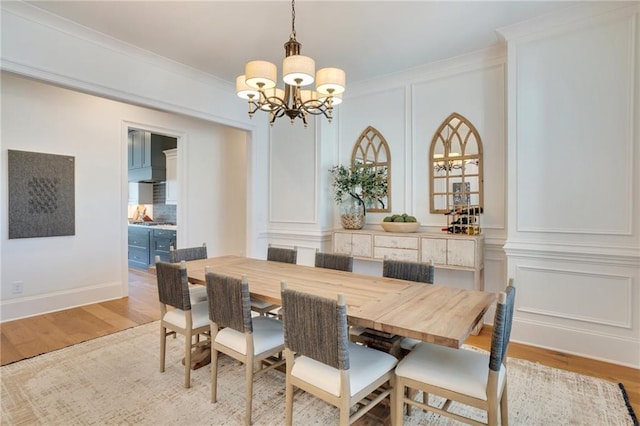 dining space with light wood-style flooring, a notable chandelier, ornamental molding, and a decorative wall