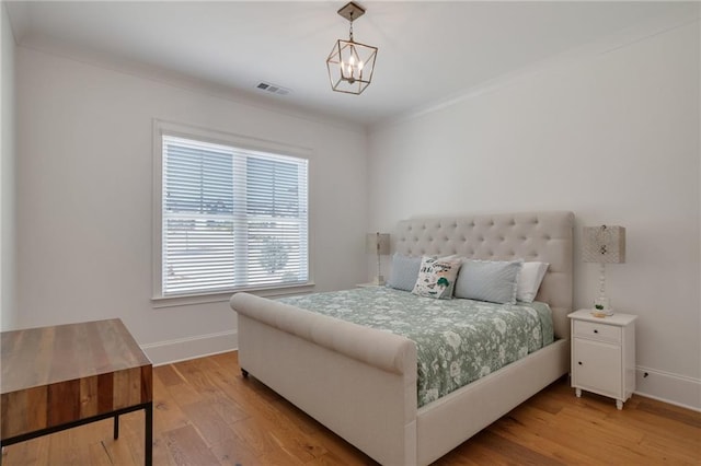 bedroom featuring light wood-type flooring, visible vents, a notable chandelier, ornamental molding, and baseboards