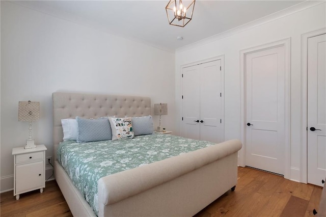 bedroom featuring two closets, light wood-style flooring, and crown molding