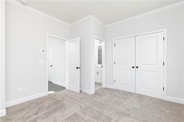 unfurnished bedroom featuring carpet floors, baseboards, ornamental molding, a closet, and ensuite bath