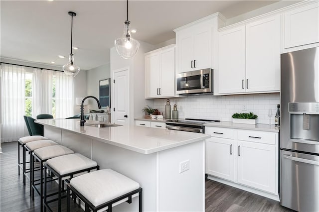 kitchen with light countertops, appliances with stainless steel finishes, a kitchen island with sink, and white cabinetry