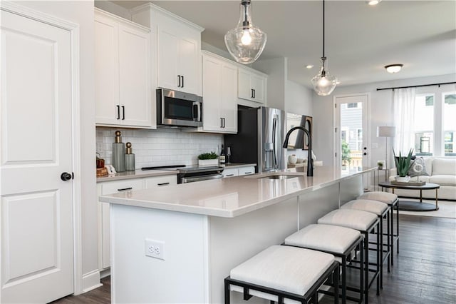 kitchen with stainless steel appliances, light countertops, a kitchen island with sink, and white cabinetry