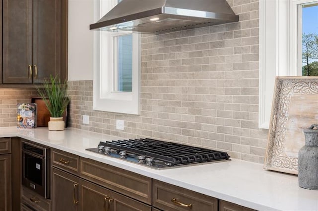 kitchen with dark brown cabinetry, decorative backsplash, wall chimney exhaust hood, and stainless steel gas cooktop