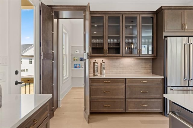 kitchen with decorative backsplash, high end fridge, dark brown cabinetry, and light hardwood / wood-style flooring