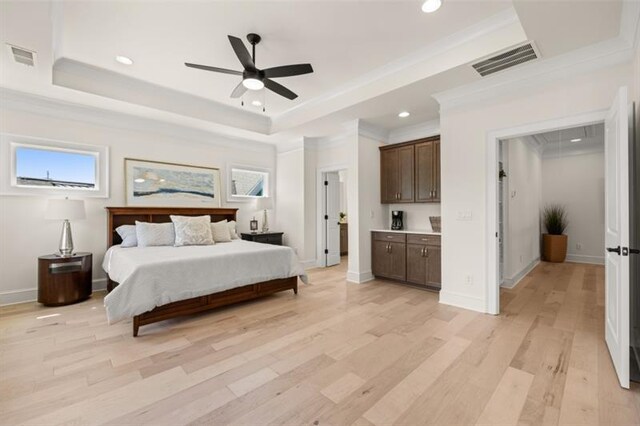 bedroom with light wood-type flooring, ensuite bath, a raised ceiling, ceiling fan, and crown molding