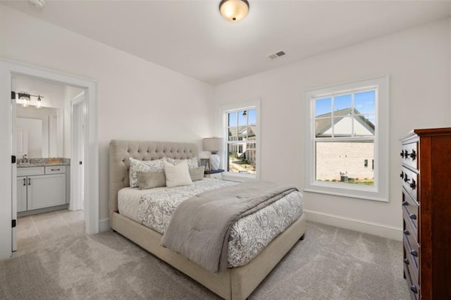 bedroom with ensuite bathroom and light carpet