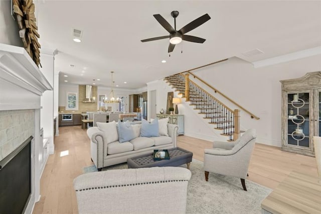 living room with ornamental molding, ceiling fan with notable chandelier, and light wood-type flooring