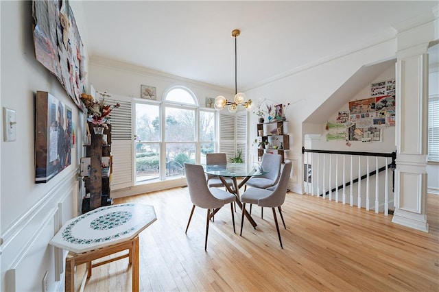 dining space with light wood-style floors, ornamental molding, a decorative wall, and an inviting chandelier