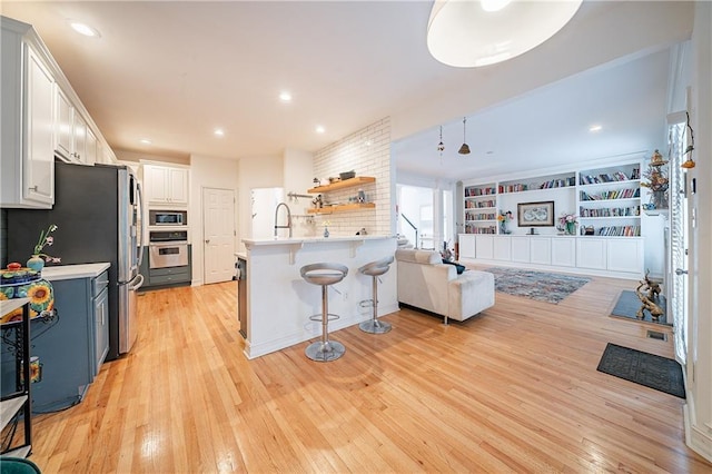 kitchen with light wood-style flooring, a peninsula, a kitchen breakfast bar, light countertops, and appliances with stainless steel finishes