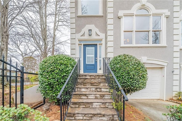 entrance to property featuring an attached garage, fence, and stucco siding