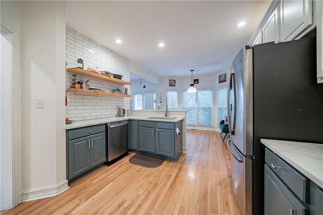 kitchen featuring stainless steel appliances, a peninsula, a sink, gray cabinets, and tasteful backsplash