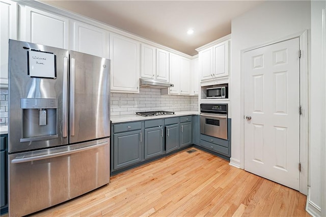 kitchen with under cabinet range hood, stainless steel appliances, white cabinets, light countertops, and gray cabinets