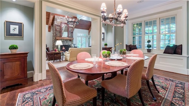 dining space with ornamental molding, a stone fireplace, dark wood-type flooring, and an inviting chandelier