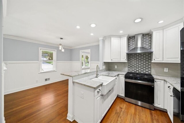 2100 Shady Ln, Tucker, GA 30084 - kitchen featuring wall chimney exhaust hood, gas stove, a peninsula, a sink, and wood finished floors
