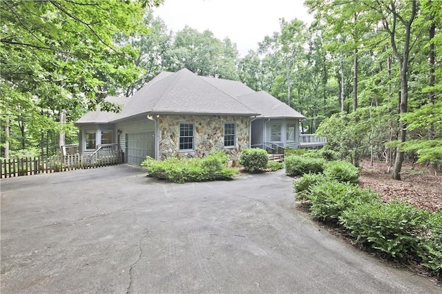 view of front facade featuring fence, driveway, a porch, a garage, and stone siding