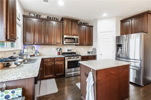 kitchen with sink, light stone counters, appliances with stainless steel finishes, a kitchen island, and dark hardwood / wood-style flooring