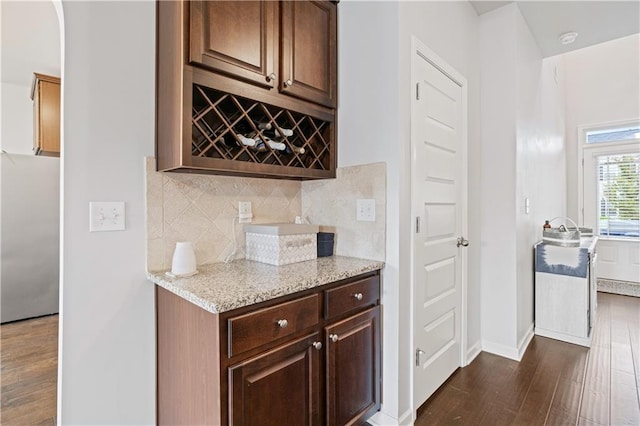 bar featuring light stone counters, dark brown cabinetry, tasteful backsplash, dark hardwood / wood-style floors, and stainless steel refrigerator