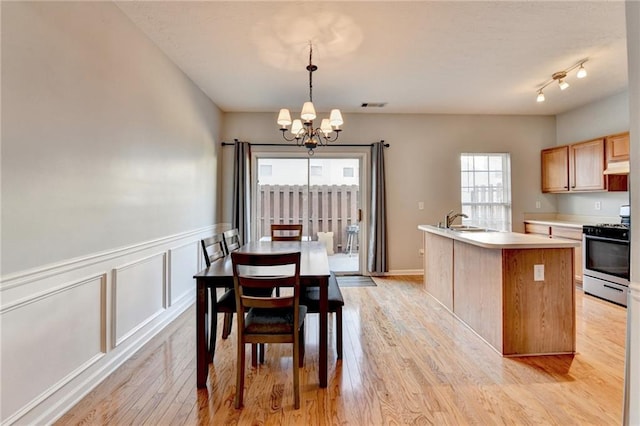 dining room with sink, light wood-type flooring, an inviting chandelier, and a wealth of natural light