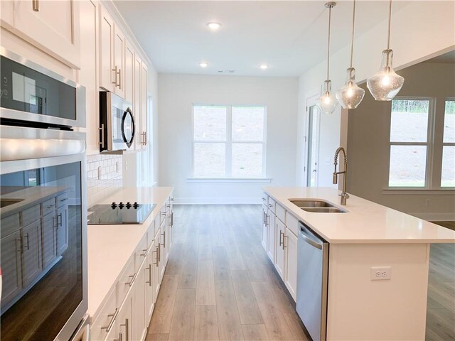 kitchen with sink, a center island with sink, white cabinetry, stainless steel appliances, and light hardwood / wood-style floors