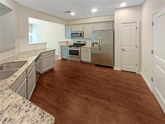 kitchen with gray cabinets, light stone countertops, appliances with stainless steel finishes, and dark hardwood / wood-style flooring