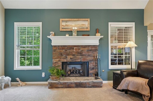 carpeted living area featuring a stone fireplace and baseboards