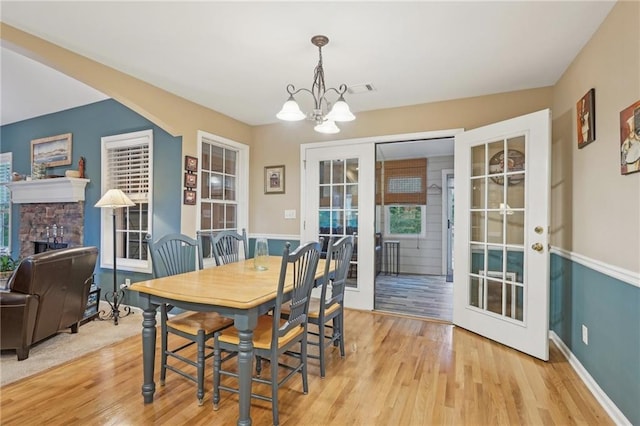 dining room with a chandelier, french doors, light wood-type flooring, a stone fireplace, and baseboards