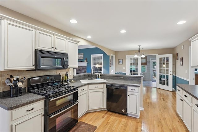kitchen with black appliances, a sink, arched walkways, dark countertops, and a peninsula