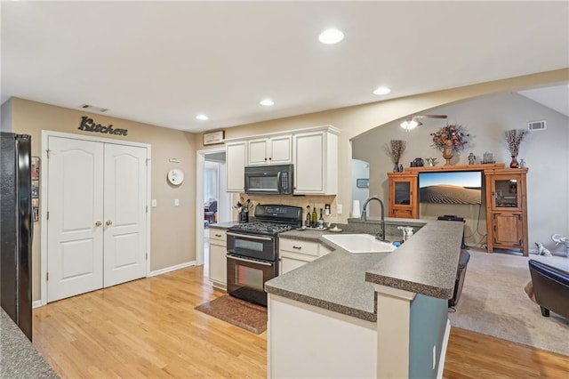 kitchen with black appliances, a sink, a peninsula, dark countertops, and arched walkways