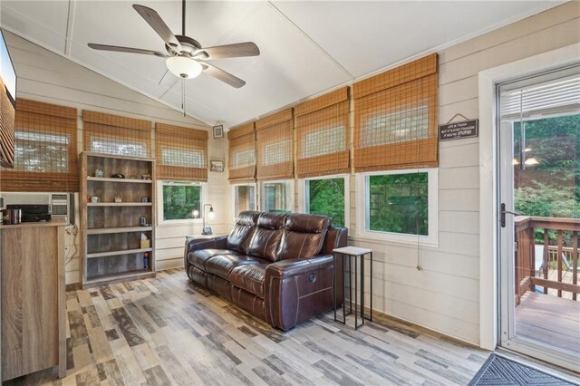 living room featuring wood finished floors, vaulted ceiling, a ceiling fan, plenty of natural light, and wooden walls