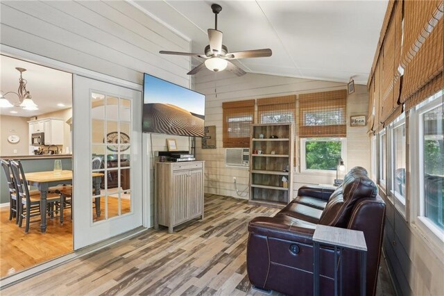 living room with wood finished floors, lofted ceiling, a ceiling fan, wooden walls, and a chandelier