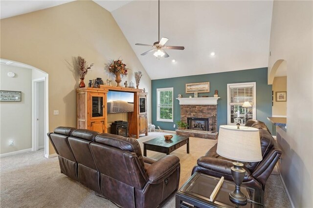 carpeted living room with arched walkways, high vaulted ceiling, ceiling fan, baseboards, and a fireplace