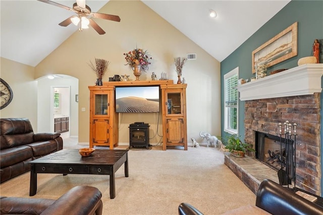living room featuring high vaulted ceiling, light colored carpet, a wood stove, arched walkways, and a ceiling fan