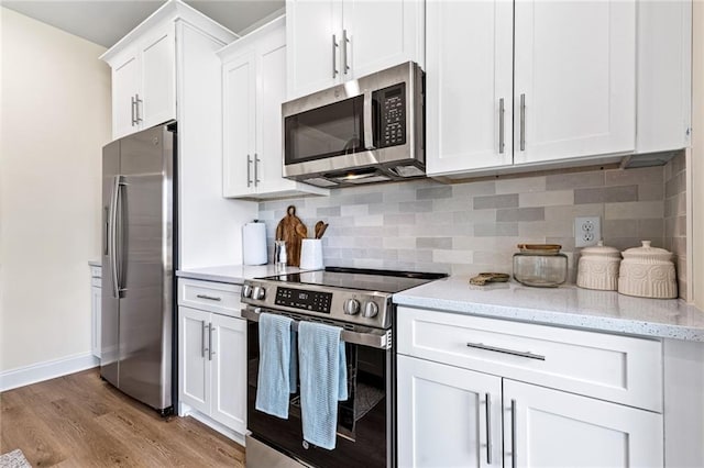 kitchen with appliances with stainless steel finishes, light wood-type flooring, white cabinets, and backsplash