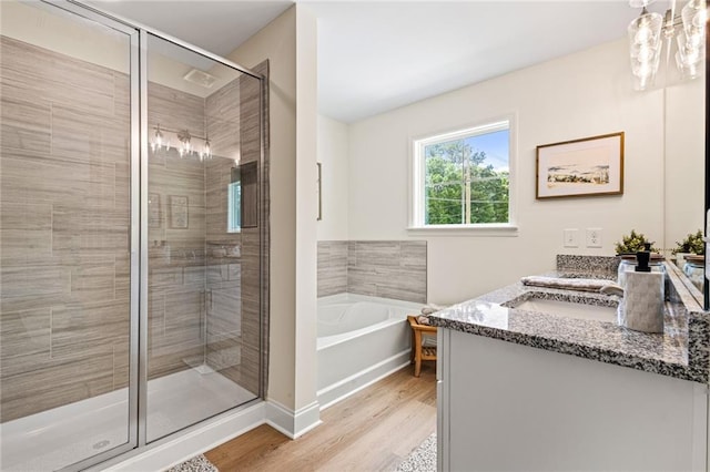 full bath featuring wood finished floors, a stall shower, a garden tub, vanity, and a chandelier