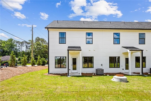 rear view of house with a lawn, an outdoor fire pit, roof with shingles, and cooling unit