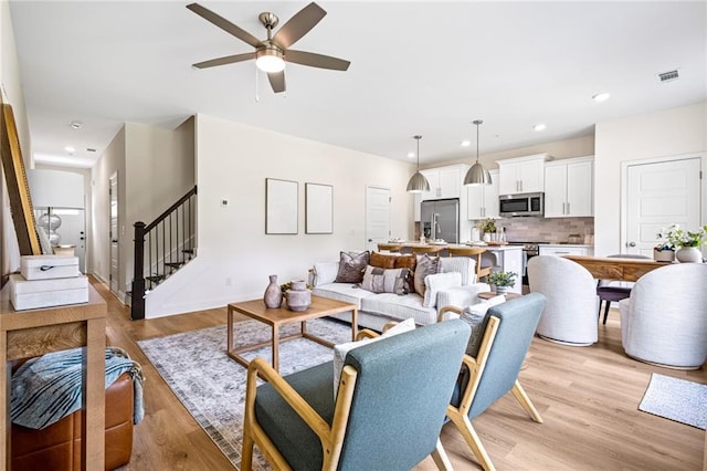 living area with stairway, ceiling fan, light wood-style floors, recessed lighting, and baseboards